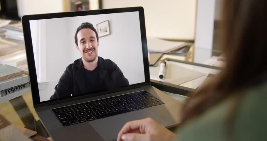 A woman sitting in an office bids farewell to a man through video chat on her laptop