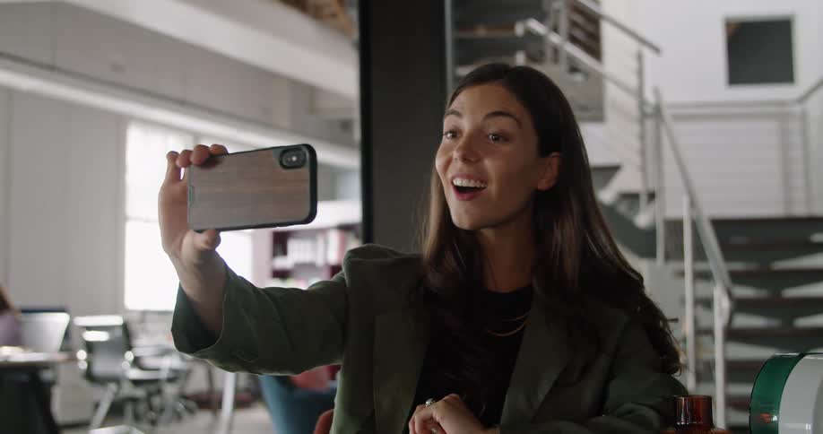 A woman holds up her cell phone and waves as she video chats with someone