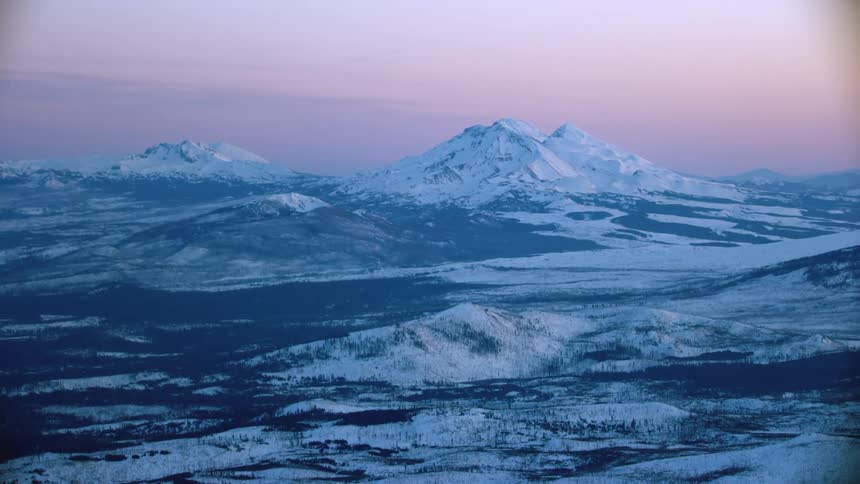 Blue hour golden light glows on the high cascade volcanoes near Bend Oregon at the peak of winter in this high altitude aerial
