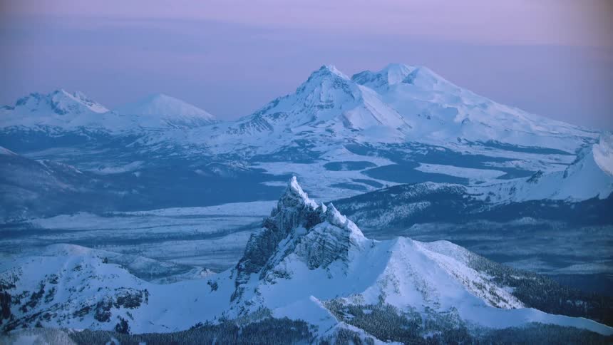 The sisters and Mount Bachelor in Oregon as well as the Cascade mountains are visible in this gorgeous blue hour sunset aerial in Oregon in winter