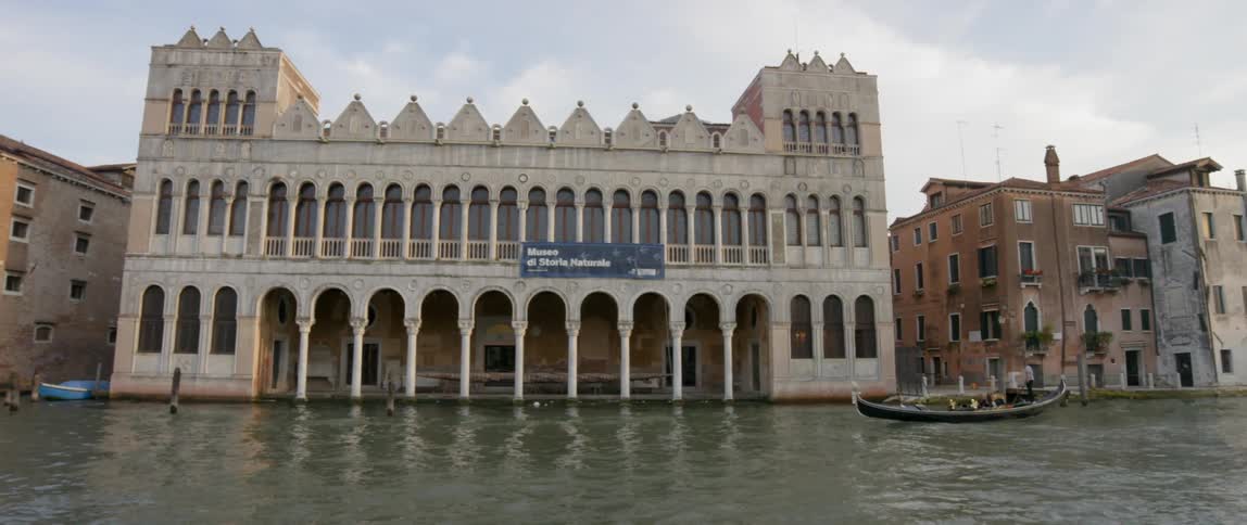 A gondolier navigates a canal in front of a building