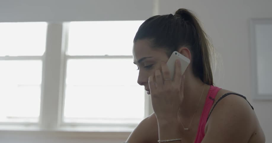 A woman sitting in a bright apartment makes a phone call on a smartphone