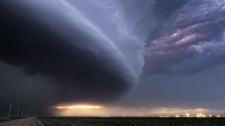 Lighting flashes from dark tornado clouds spinning in the air over a rural area