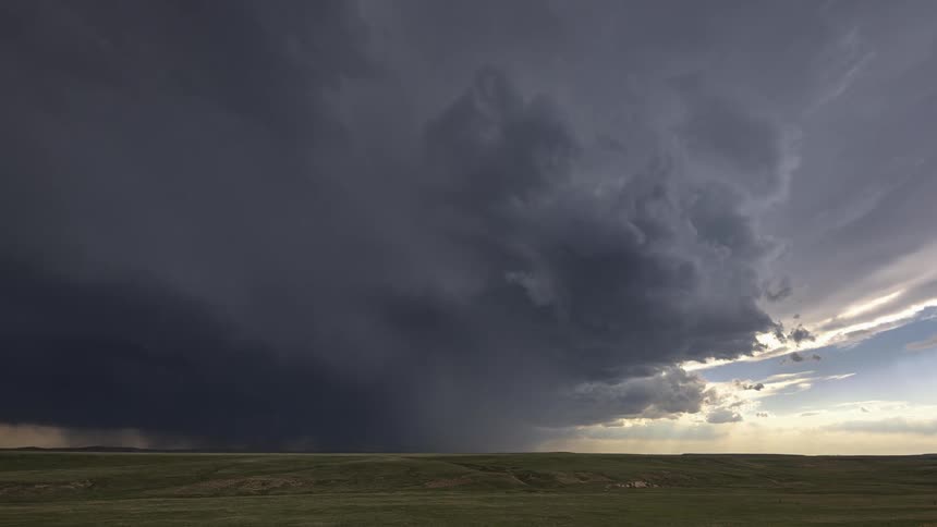 Timelapse of rain and dark storm clouds rolling over a field at sunset
