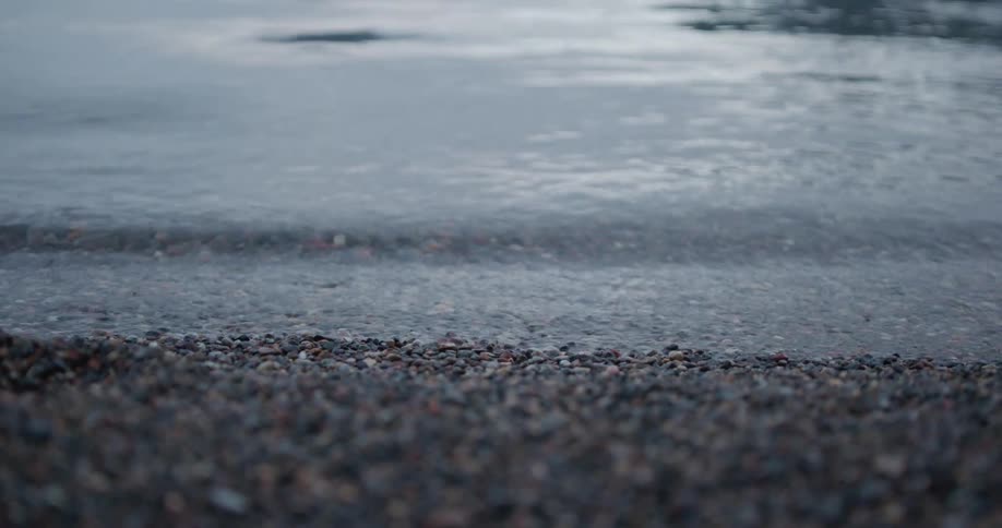 Waves washing up on a shore with gravel and the water reflecting the sky