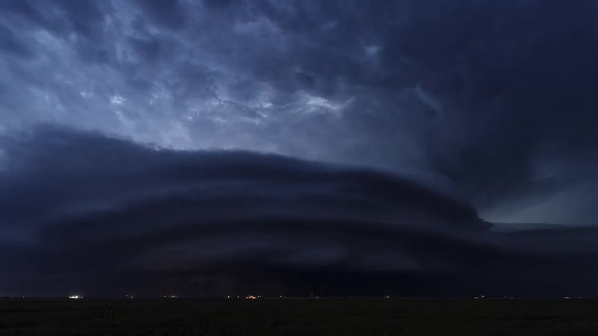 Lighting flashes from dark tornado clouds spinning in the air over farmland