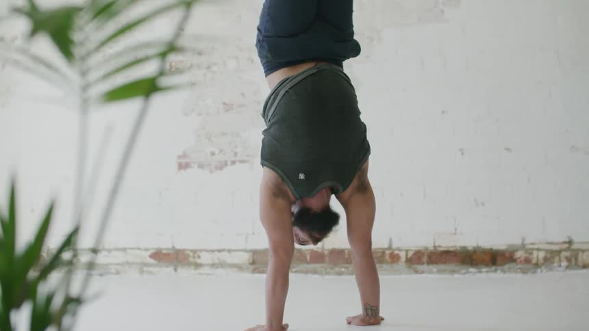 A man goes in to handstand position and then moves his legs as he keeps his balance