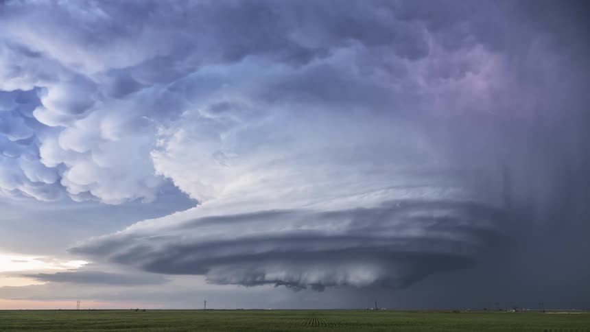 Lighting flashes from tornado clouds spinning in the air over farmland
