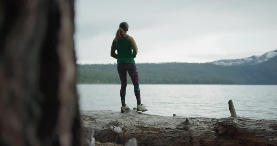Young woman with a standing on the shore of a lake near the pine tree forest in the mountains