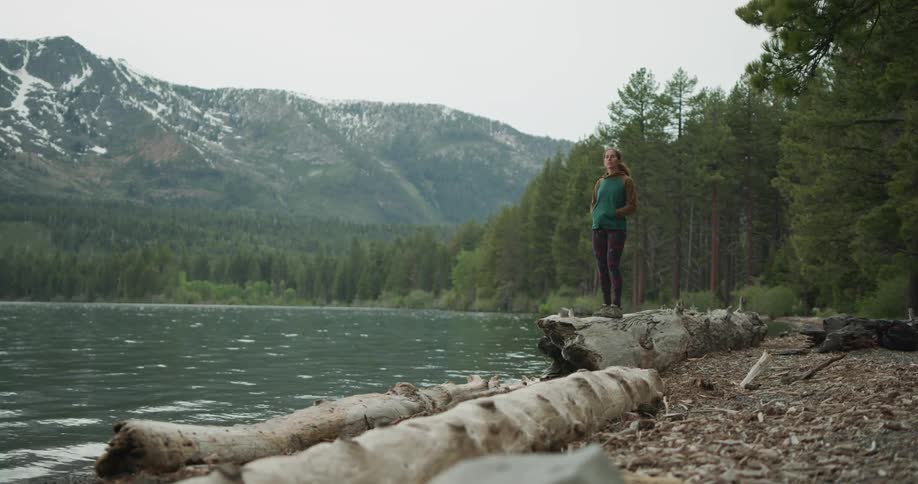 Woman standing on log at lakes shoreline in the wilderness enjoying the scenery