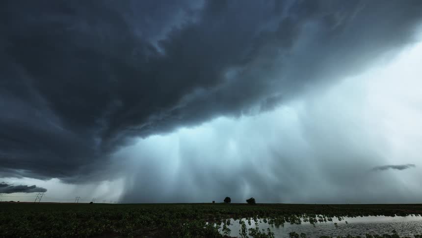 Storm clouds burst over a green level landscape and pond