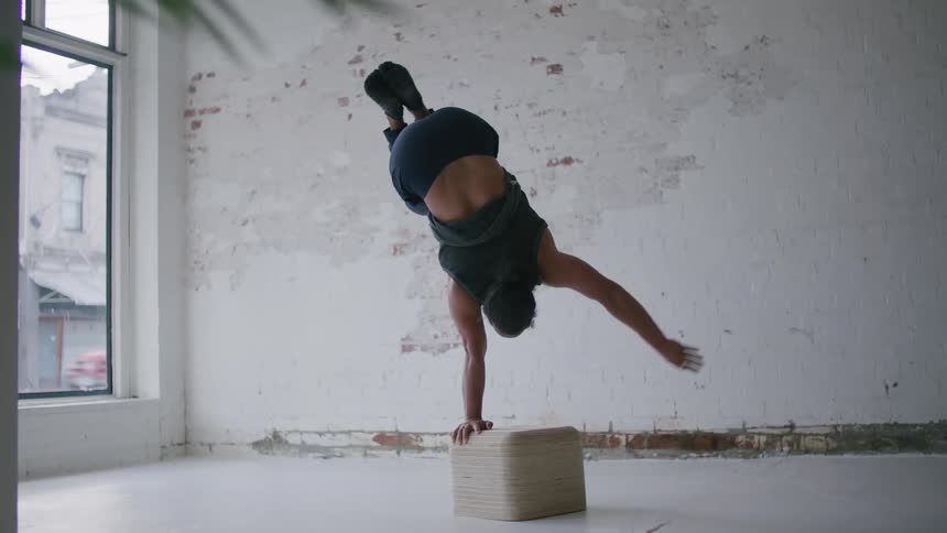 Bearded man wearing sports clothes doing yoga balances standin on his hands inside a room