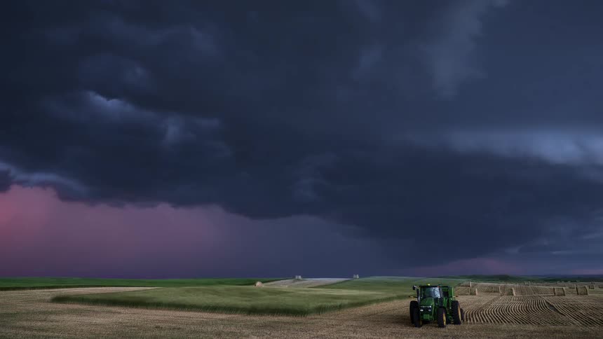 Lightning flashes as dark storm clouds move over a tractor on a farm