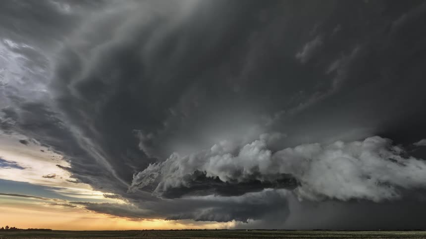 Timelapse of rain and dark storm clouds rolling over a field at sunset