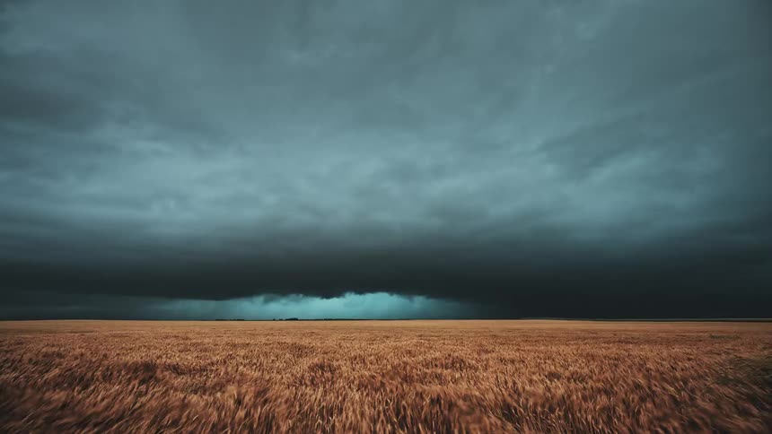 Dark storm clouds floating over a rural grassy field during a rainstorm
