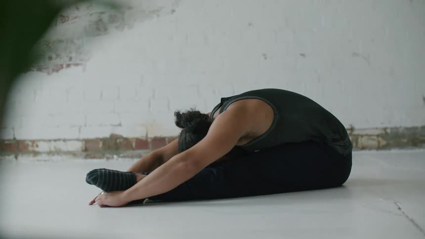 Bearded man wearing sports clothes doing yoga stretches on the floor of a room