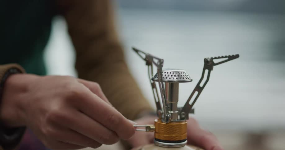 Woman setting up a small camping stove near a lake
