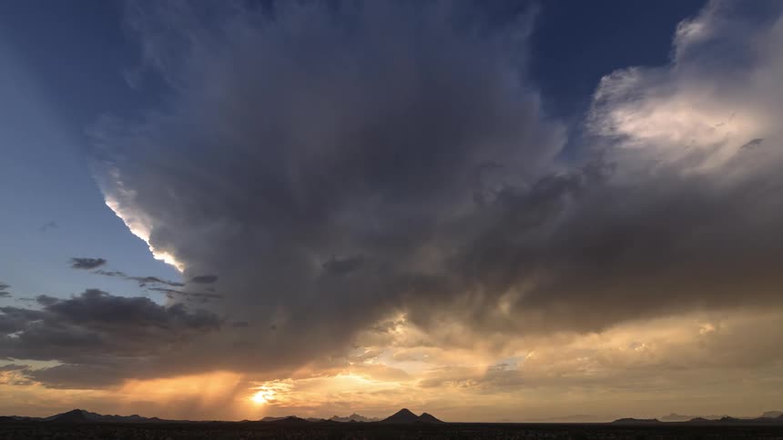 Timelapse of rain and dark storm clouds rolling over a field at sunset