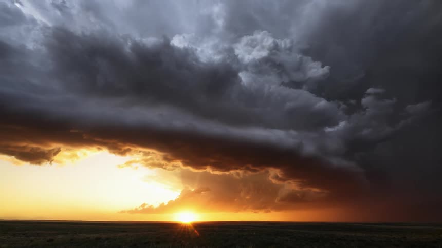 Lightning strikes the ground as thick storm clouds pass over a vast grassland at sunrise