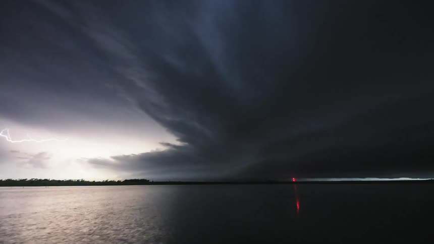 Timelapse of lightning and dark storm clouds rolling over a lake at evening