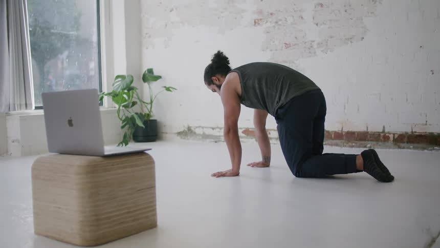 A man doing yoga in front of a laptop