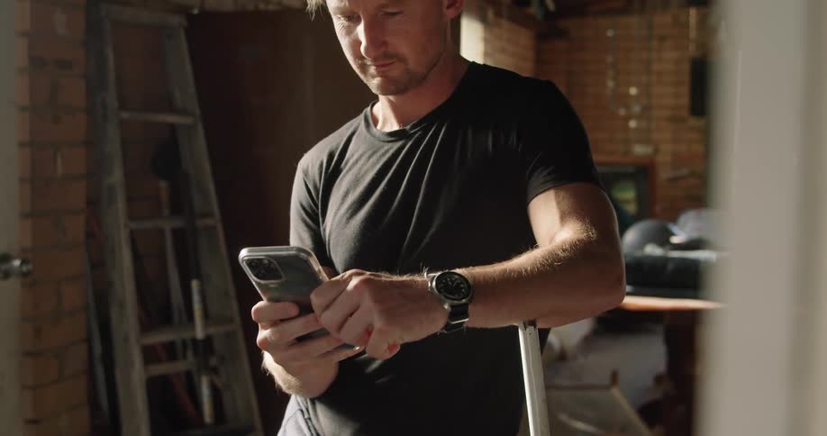 A man smiles after sending a text on his smartphone while standing in his home