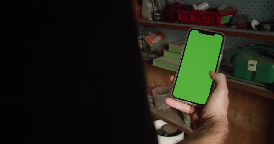 A man scrolls through a green screen on a smart phone indoors