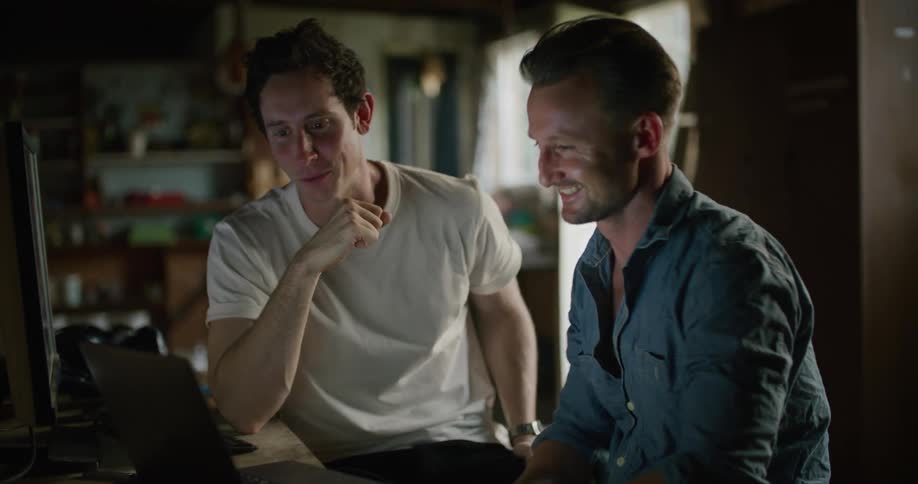 Two men talk and look at a laptop and then fist bump one another