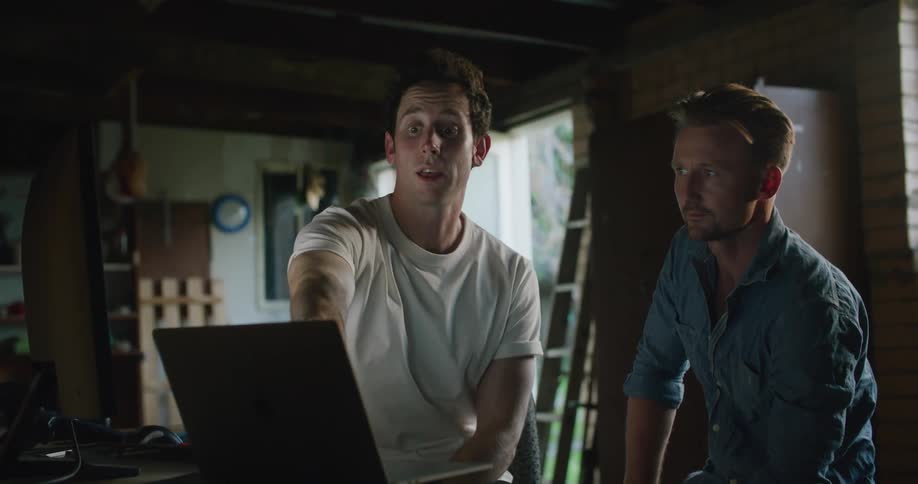 Two men on a meeting inside a dimly lit room talking to each other pointing at a laptop
