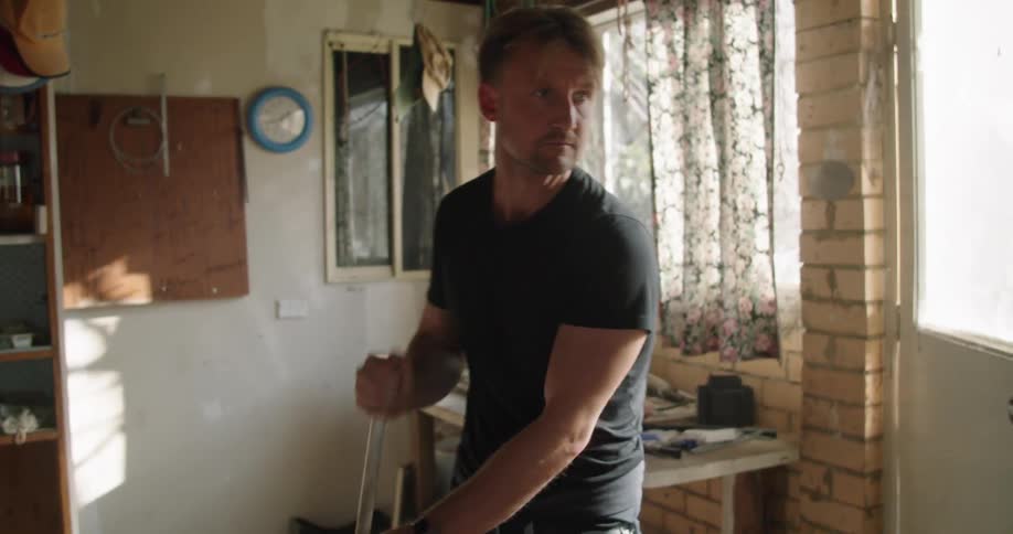 A man uses a broom to sweep a pile of dust and debris together in a room then stops to look around