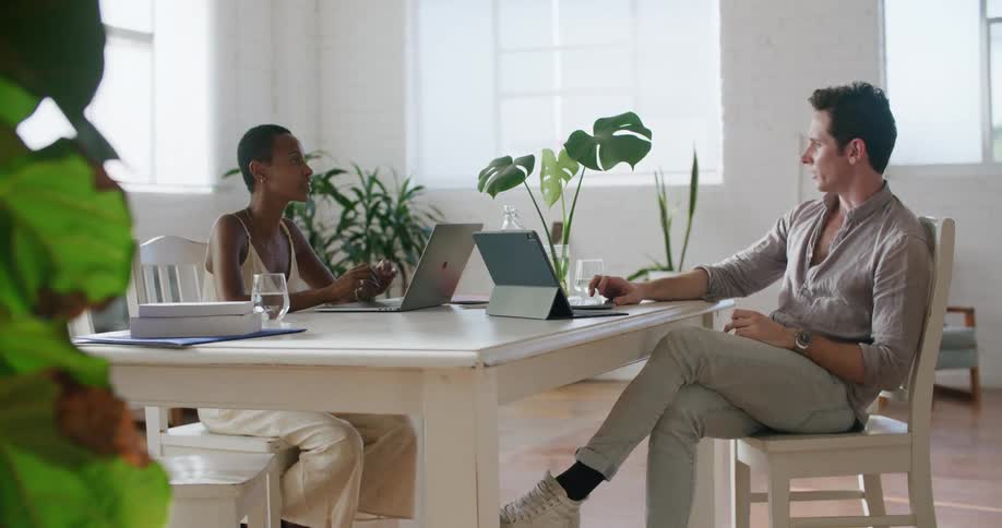 A man and woman in an office sit at desk with computers in front of them and talk