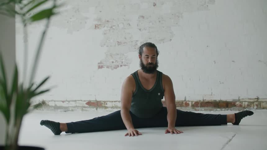 Bearded man wearing sports clothes doing yoga stretches on the floor of a room