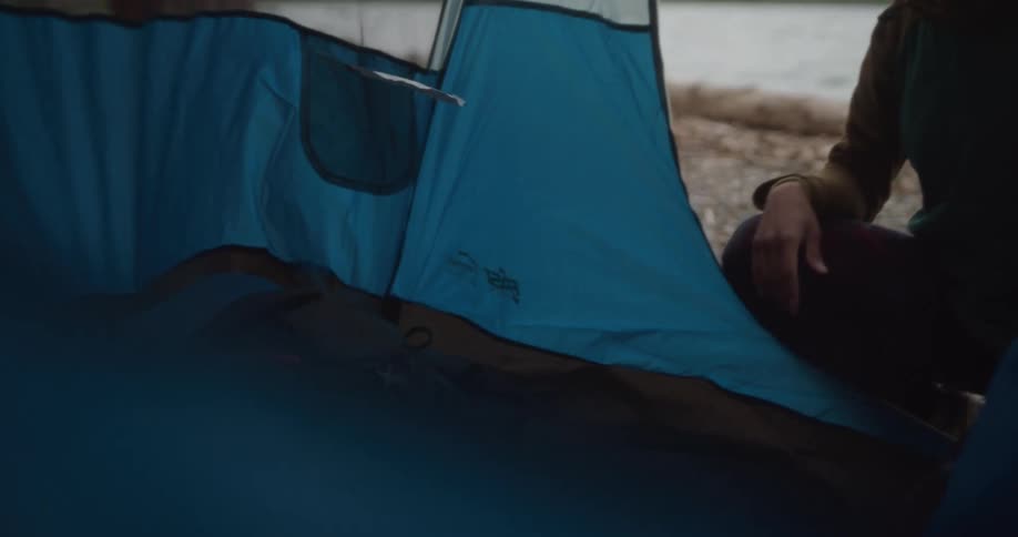 A woman places a backpack inside a lakeside tent