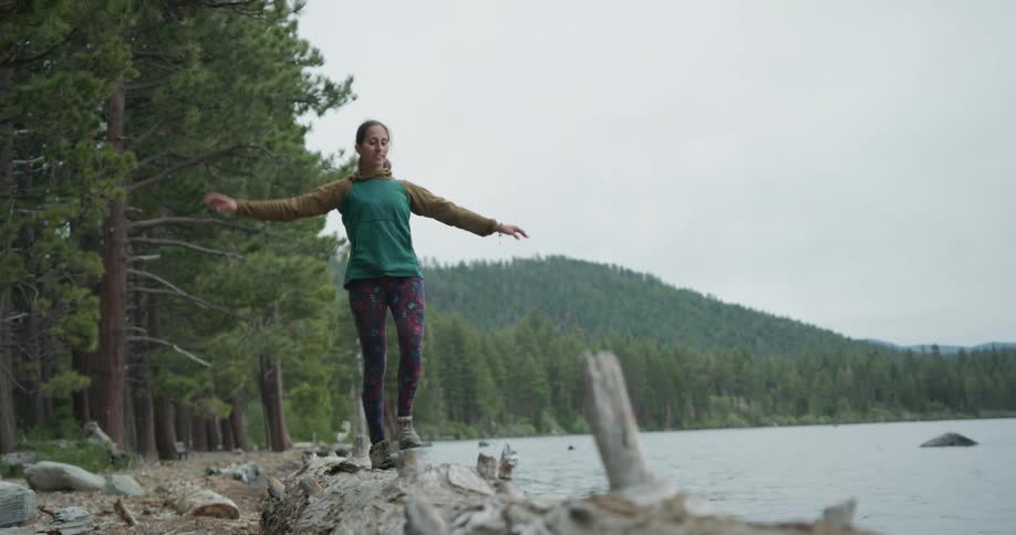 A woman steadies herself as she walks along rocks on the shore