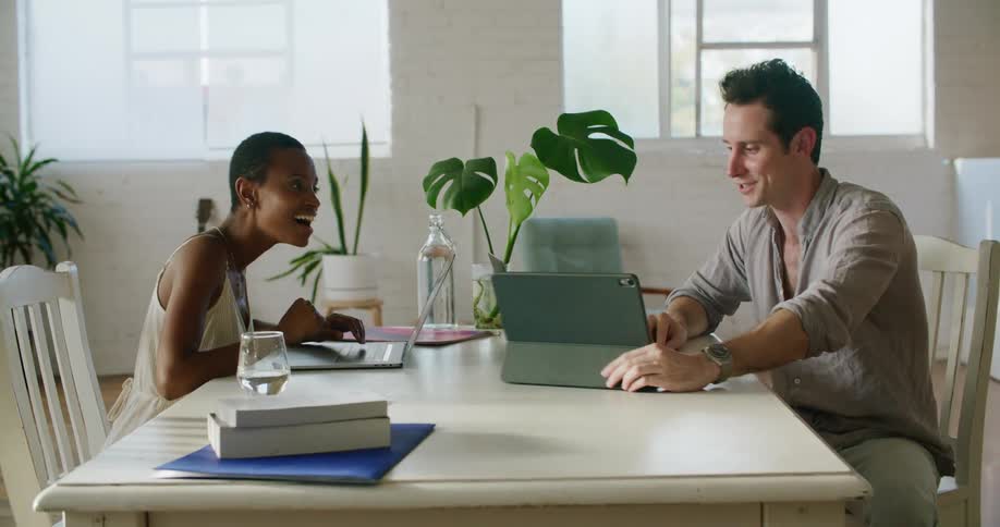 A man and woman sit at a table with computers and excitingly high five each other for an accomplishment