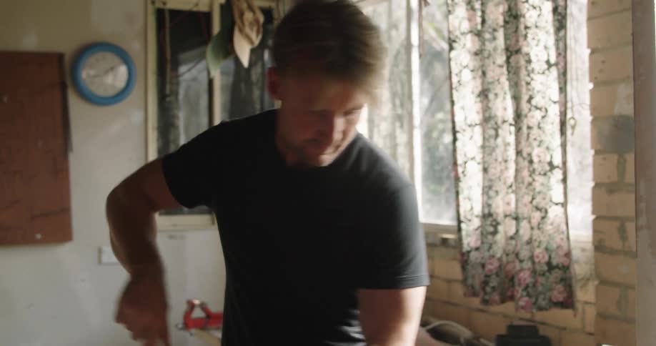 Blonde man with a black t shirt and jeans talks on the smartphone and sweeps the garage