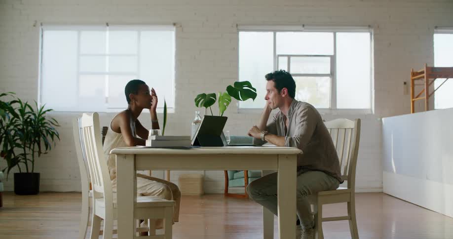A man and woman talk sitting at a table together with computers