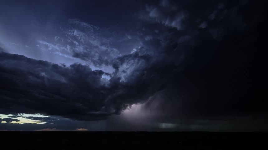 A time lapse shows enormous storm clouds with lightning flashes in the sky at sunset