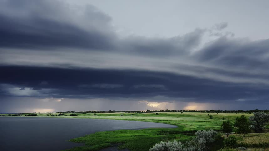 Timelapse of rain and dark storm clouds rolling with lightning over a field at sunset