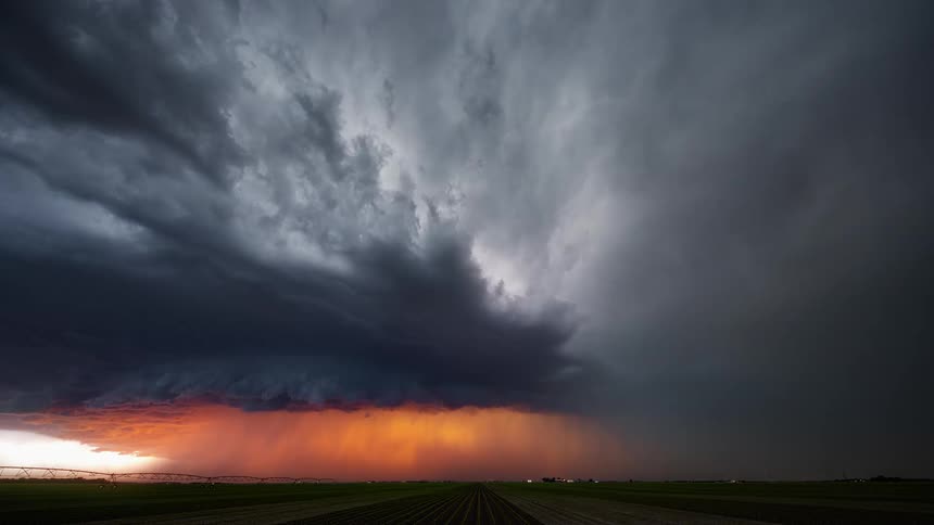 Storm front flows over fields as traffic flows along road toward buildings