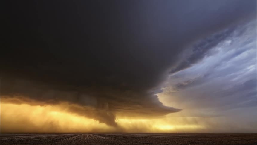 Timelapse of rain and dark storm clouds rolling over a field at sunset