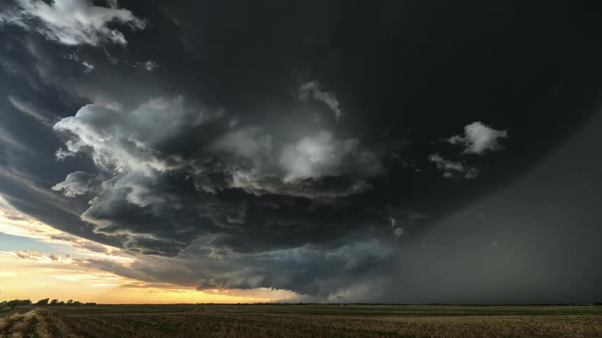 Timelapse of rain and dark storm clouds rolling over a field at sunset