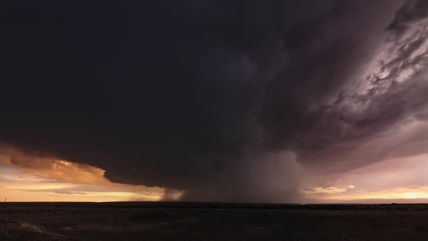 Lightning flashes from dark tornado clouds spinning in an orange sky over farmland