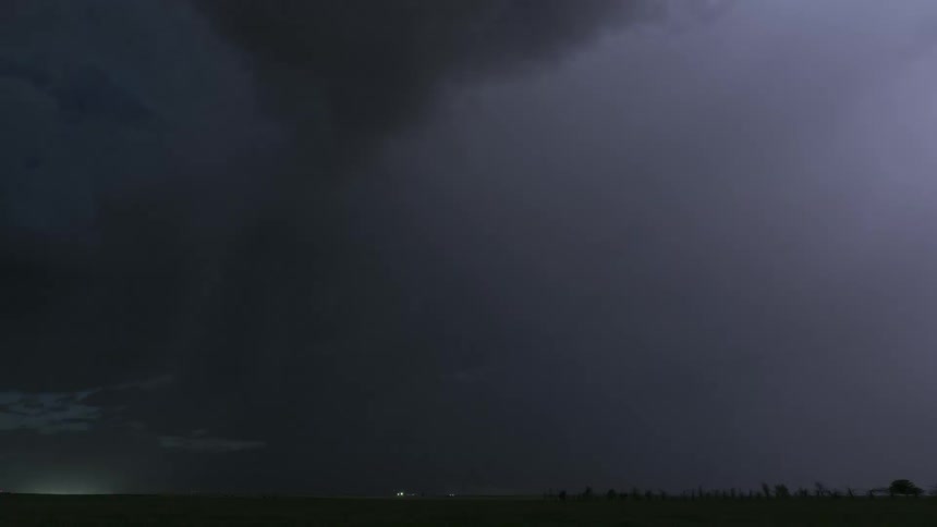 Timelapse of lightning and dark storm clouds rolling over a field at night