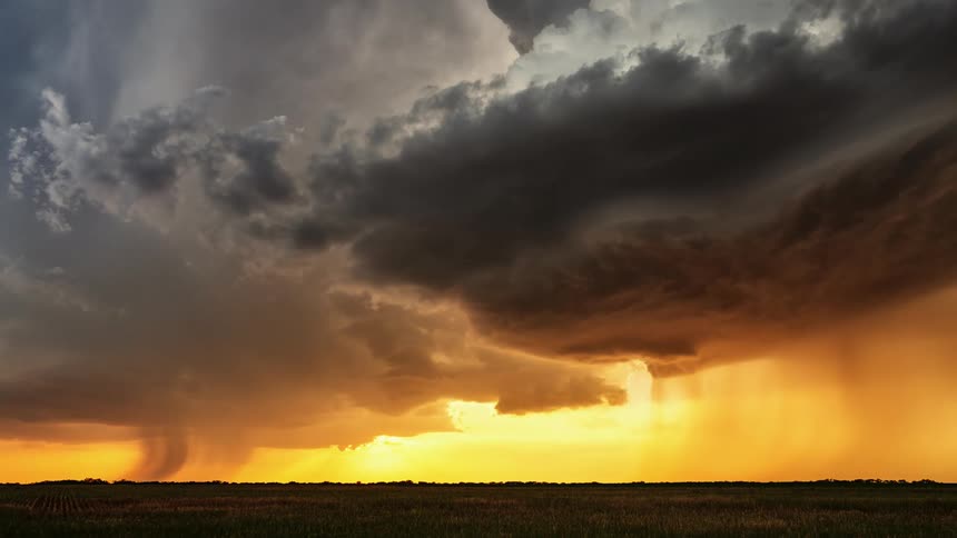 Dark storm clouds move across a bright orange sky