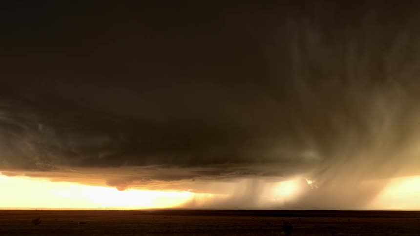 Dark storm clouds swirling over a rural field during a rainstorm at sunset