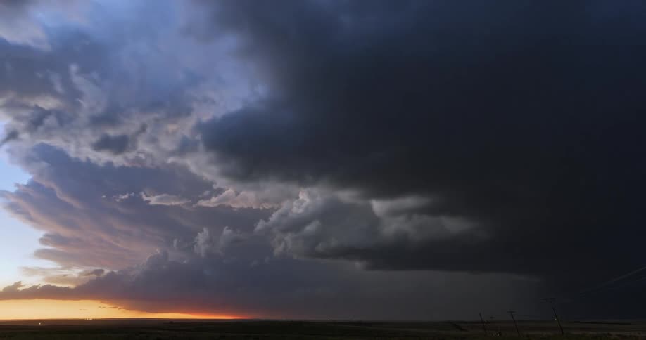 Timelapse of lightning and dark storm clouds rolling over a field at sunset