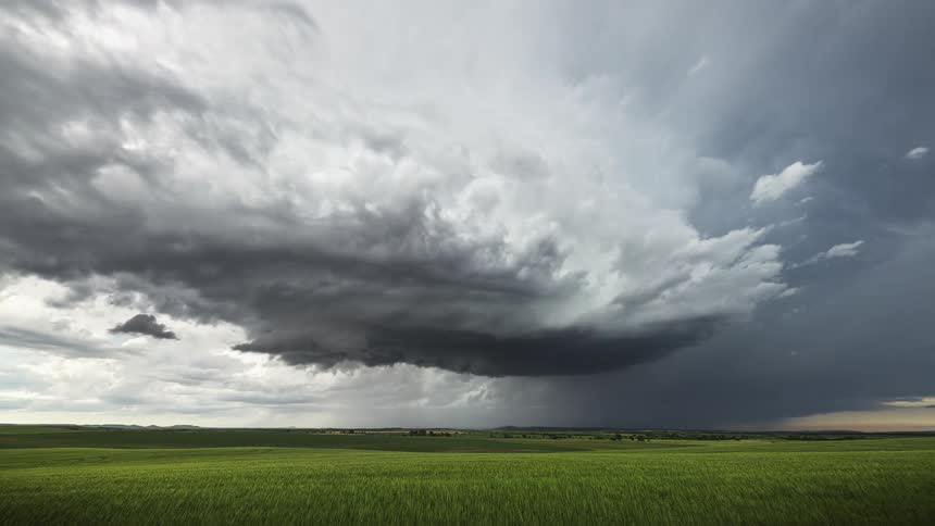 Dense clouds spin as the sky darkens over a vast green field