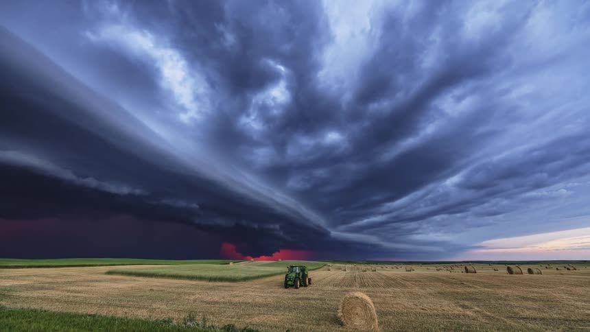 Black clouds with lightning flow across partly harvested hay field