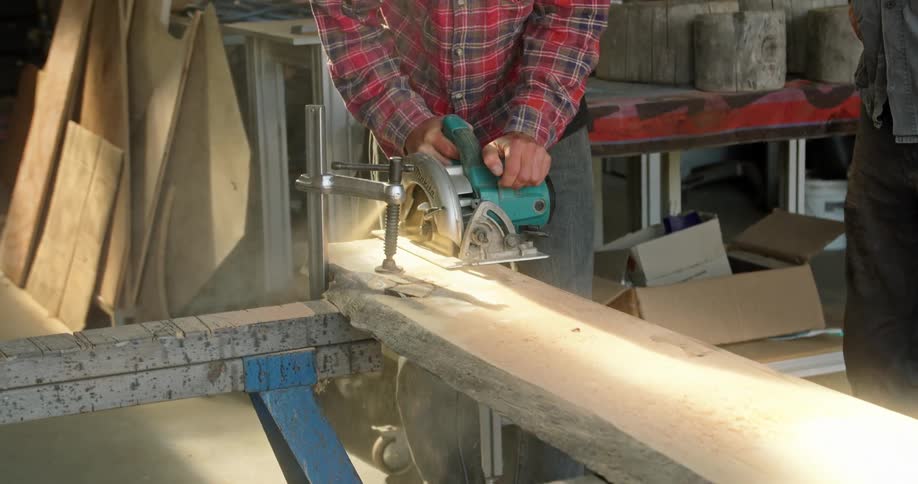 Two men in a woodworking workshop cutting lumber using power tools
